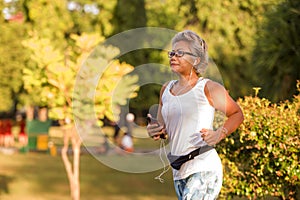 Middle aged 40s or 50s happy and attractive woman with grey hair training at city park with green trees on sunrise doing running