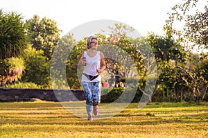 Middle aged 40s or 50s happy and attractive woman with grey hair training at city park with green trees on sunrise doing running