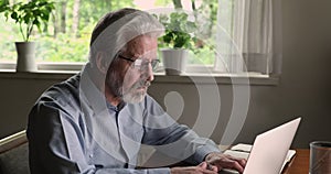 Middle aged 55s man sit at desk typing on laptop
