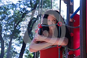 Middle-aged adult Hispanic woman with black curly hair, hugging the ropes of a climbing apparatus, angry. Concept games, anger,