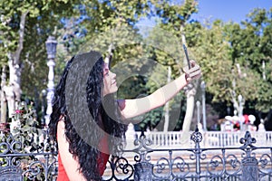 Middle-aged adult Hispanic woman with black curly hair taking a photo with her cell phone. Technology and selfie concept