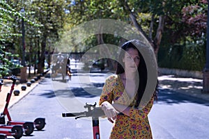 Middle-aged adult Hispanic woman with black curly hair, wearing a colorful outfit, leaning on an electric scooter. Concept scooter