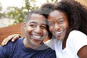 Middle aged African American  dad and teenage daughter embracing and smiling to camera, close up