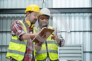 Middle aged African engineer and Asian foreman in safety hat working together at warehouse while listing on clipboard to discuss,