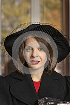 Middle-aged aristocrat woman looks arrogantly into camera. Portrait of woman in retro clothes, wide-brimmed black hat