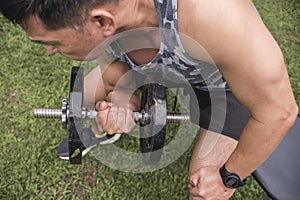 A middle aged asian guy exercising outdoors. Doing concentration bicep curls on a bench. Arm workout