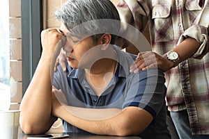 Middle-aged Asian man 40 years old, stressed and tired, are sitting in fast food restaurant and have friends standing behind to en