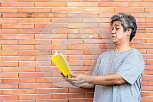 Middle-aged Asian man has gray hair, is reading a book By holding it away from the eyes, because he has farsightedness photo