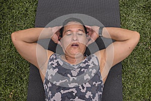 A middle aged asian man struggles to do a set of ab crunches on mat at his yard outdoors. Exhausted and tired