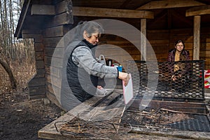 A middle-aged Asian woman cooking Souvlakia at a campsite fireplace.