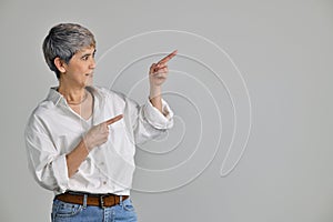 Middle aged Asian woman pointing fingers up at empty copy space for text isolated on white background