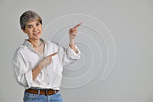 Middle aged Asian woman pointing fingers up at empty copy space for text isolated on white background