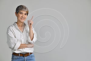 Middle aged Asian woman pointing fingers up at empty copy space for text isolated on white background