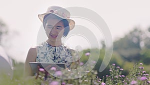 Middle aged asian woman using a tablet while checking the quality of flowers in garden