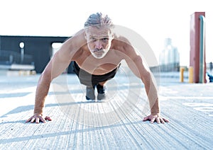 Middle-aged athletic man doing push ups outdoors. Fitness and exercising outdoors urban environment.