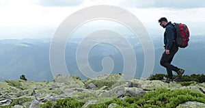 A middle-aged backpacker man slowly approaches the edge of a mountain