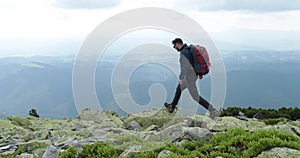 A middle-aged backpacker man slowly approaches the edge of a mountain