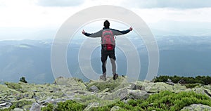 A middle-aged backpacker man slowly approaches the edge of a mountain