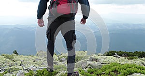 A middle-aged backpacker man slowly approaches the edge of a mountain