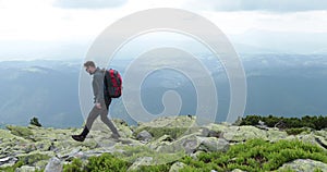 A middle-aged backpacker man slowly approaches the edge of a mountain