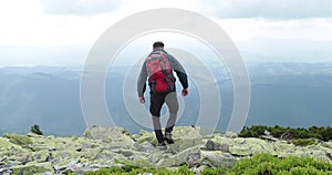 A middle-aged backpacker man slowly approaches the edge of a mountain