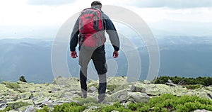 A middle-aged backpacker man slowly approaches the edge of a mountain