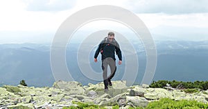 A middle-aged backpacker man slowly approaches the edge of a mountain