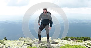 A middle-aged backpacker man slowly approaches the edge of a mountain