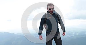 A middle-aged backpacker man slowly approaches the edge of a mountain