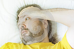 A middle-aged bearded man lies on a pillow in the early morning