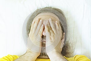 A middle-aged bearded man lies on a pillow in the early morning and rubs his eyes after sleeping