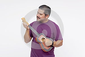 A middle aged bearded man playing the ukelele. Strumming a small guitar. Isolated on a white background