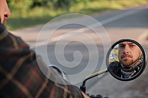 A middle aged biker man looks in the rearview mirror and rides a motorcycle