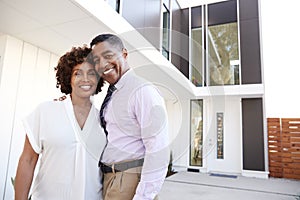 Middle aged African American  couple stand outside admiring their modern home, back view photo
