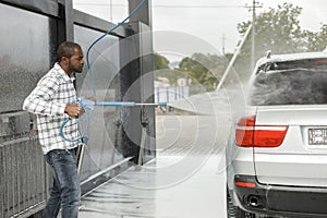 Middle aged black man cleaning his car outside in the car wash