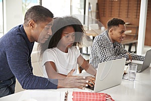 Middle aged African American  man helping his teenage children do their homework using laptop computers