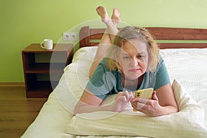 Middle aged blond hair woman using mobile phone in bed