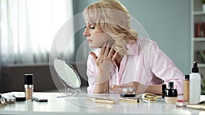 Middle-aged blond woman applying expensive makeup at home, anti-aging cosmetics