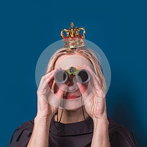 A middle-aged blonde woman with a crown on her head looks through binoculars and makes plans for the future