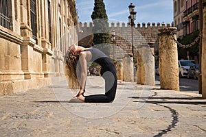 Middle-aged blonde woman, wearing a black bodysuit, doing meditation and yoga exercises in the historical center of the city.