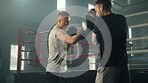 Middle-aged boxer striking boxing round punch shield held by man in gym
