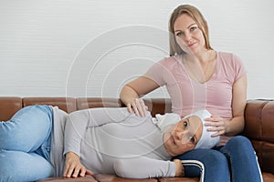 A middle-aged breast cancer woman with clothing around her head affected from chemotherapy lie on her daughter`s lap with