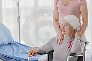 A middle-aged breast cancer woman with clothing around her head effected from chemo therapy sitting on wheel chair and hold hand