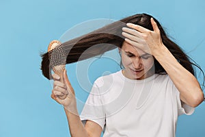 middle-aged brunette woman combing her long beautiful hair with a wooden comb and screaming loudly in pain while
