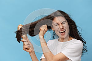 middle-aged brunette woman combing her long beautiful hair with a wooden comb and screaming loudly in pain while