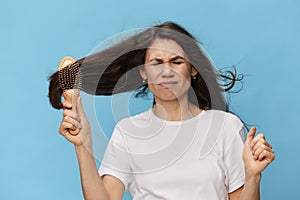 middle-aged brunette woman combing her long beautiful hair with a wooden comb and screaming loudly in pain while