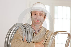 middle-aged builder with reel grey conduit on shoulder