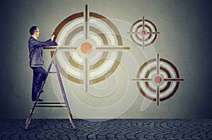 Middle aged business man on a ladder drawing a target on a wall