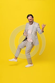 Middle aged business man musician pretend playing guitar happy smiling isolated on yellow background. Handsome mature
