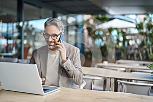 Middle aged business man talking on phone working on laptop outdoors. Copy space